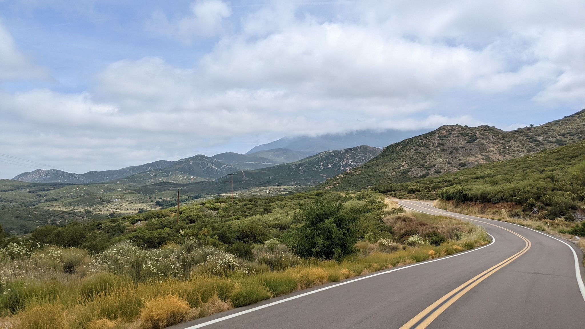 Winding road through green hills under a partly cloudy sky. - Boulder Creek Road