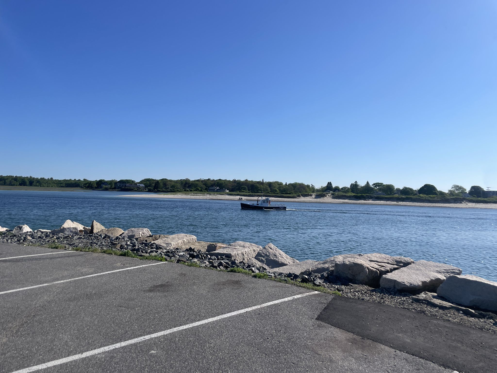 A boat navigates a sunny channel with rocky shores and distant trees. - Atlantic Avenue via Harbor Road