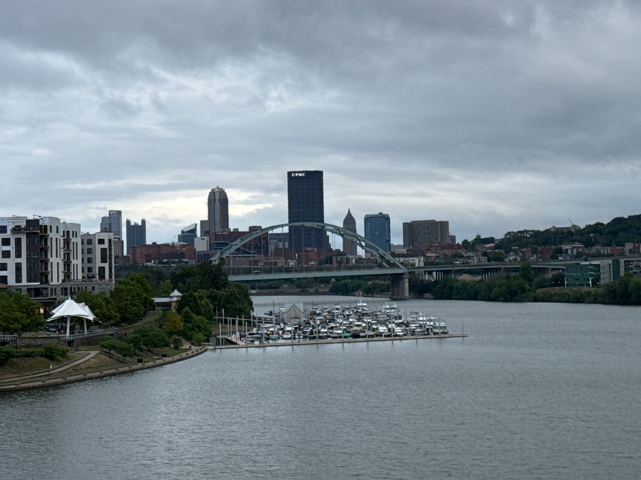 River with a marina, city skyline, and arched bridge under cloudy skies. - Hot Metal Bridge – North Shore Riverfront Park loop from Perry South