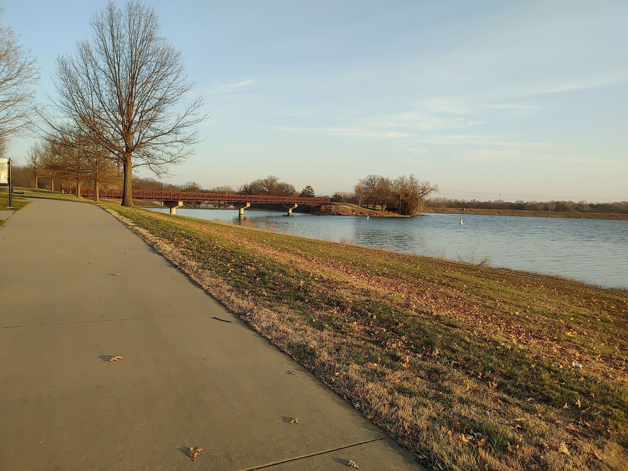 Paved path next to a lake with a distant bridge under golden light. - Lake Shawnee Trail