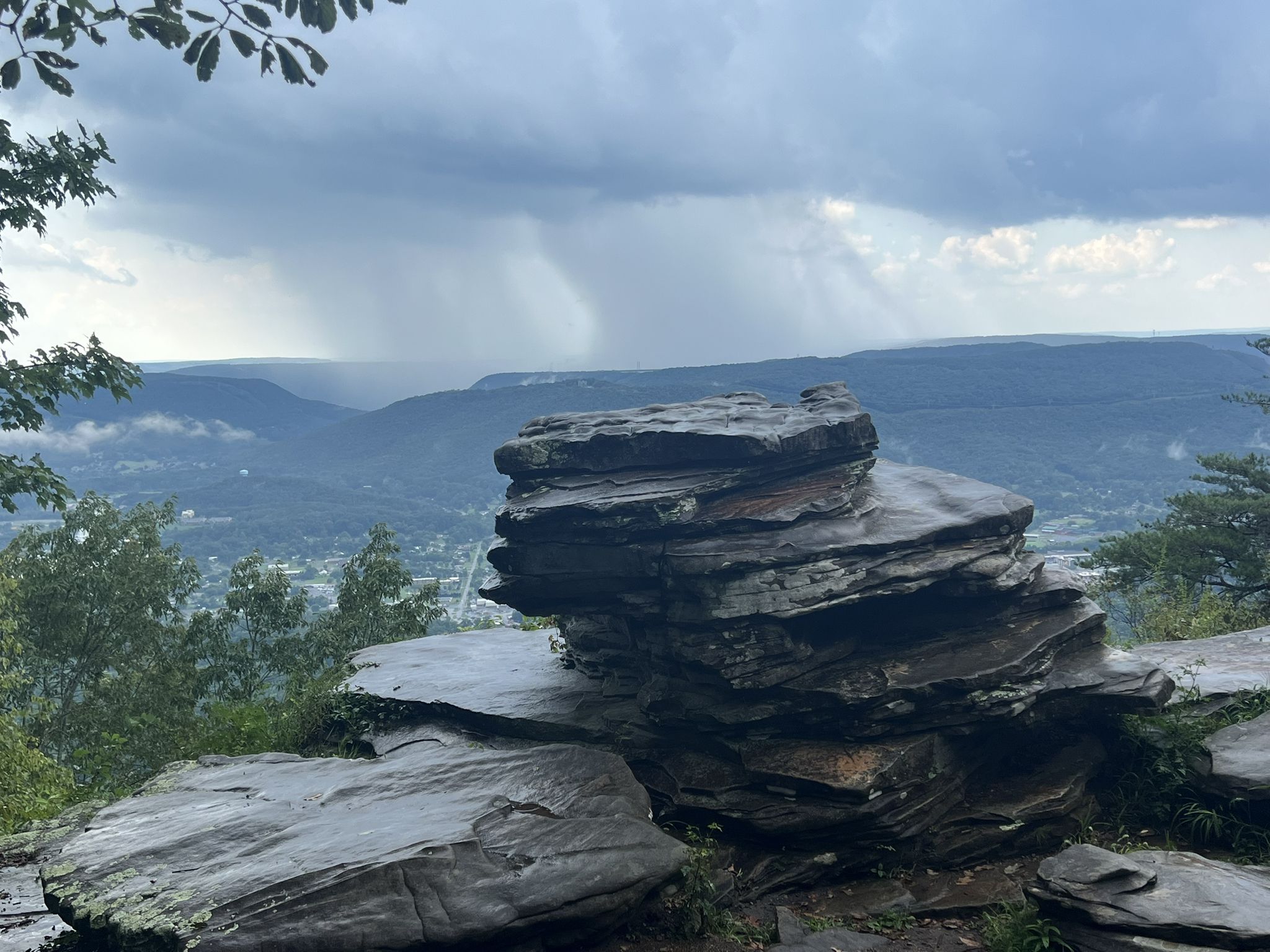Stacked rock formations on a cliff edge overlooking a valley with distant rain. - Mountain Beautiful, Hardy, and Glen Falls Trail Loop