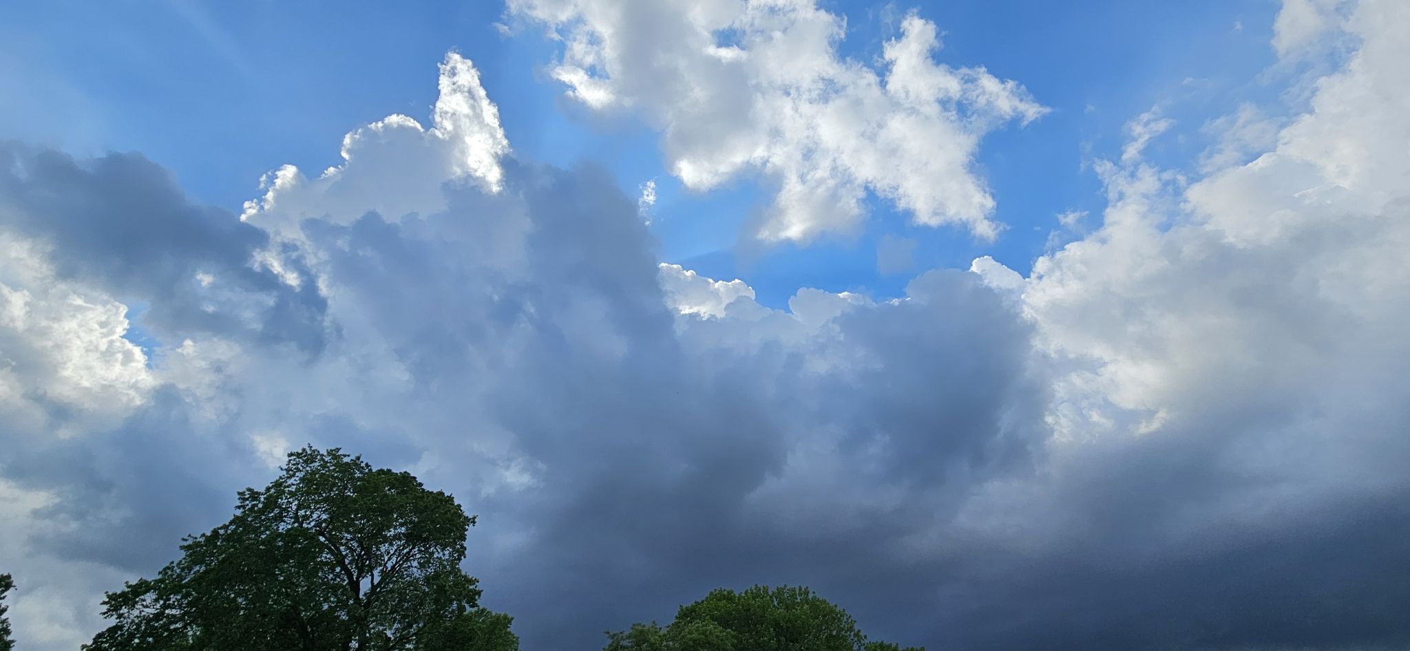 Dramatic sky with bright sun peeking through fluffy and dark clouds. - Creekside Trail