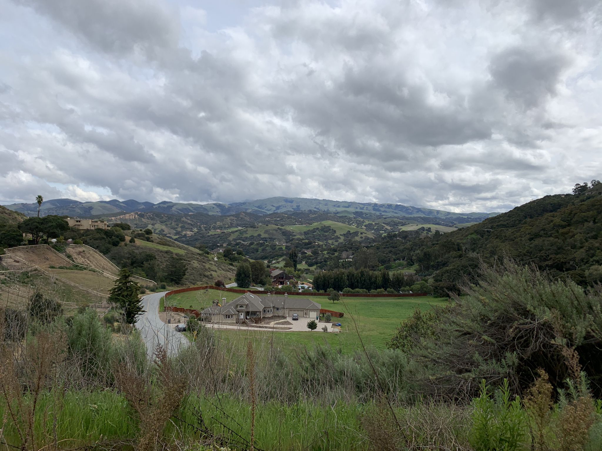 A large house sits in a green valley surrounded by distant hills. - Roadbike loop from WeatherTech Raceway Laguna Seca