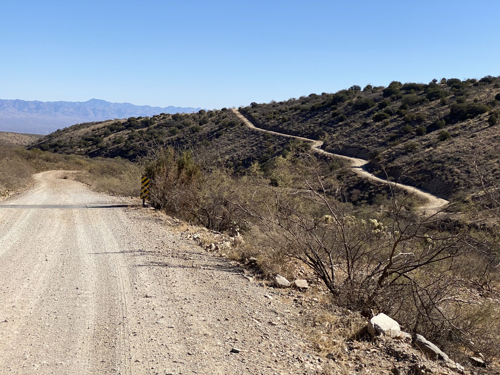 Gravel road winding up a dry, brush-covered hillside under a clear sky. - Mt. Lemmon loop via North Control Road
