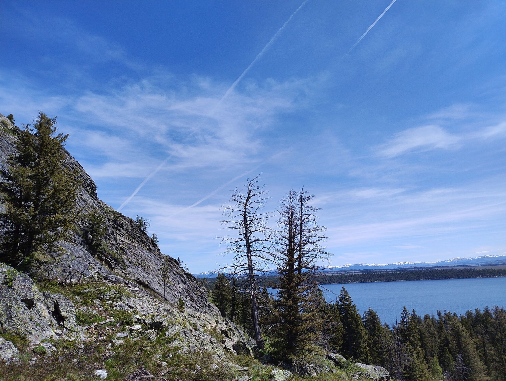 Bright blue sky with contrails over a lake, forest, and rocky hillside. - Inspiration Point Trail