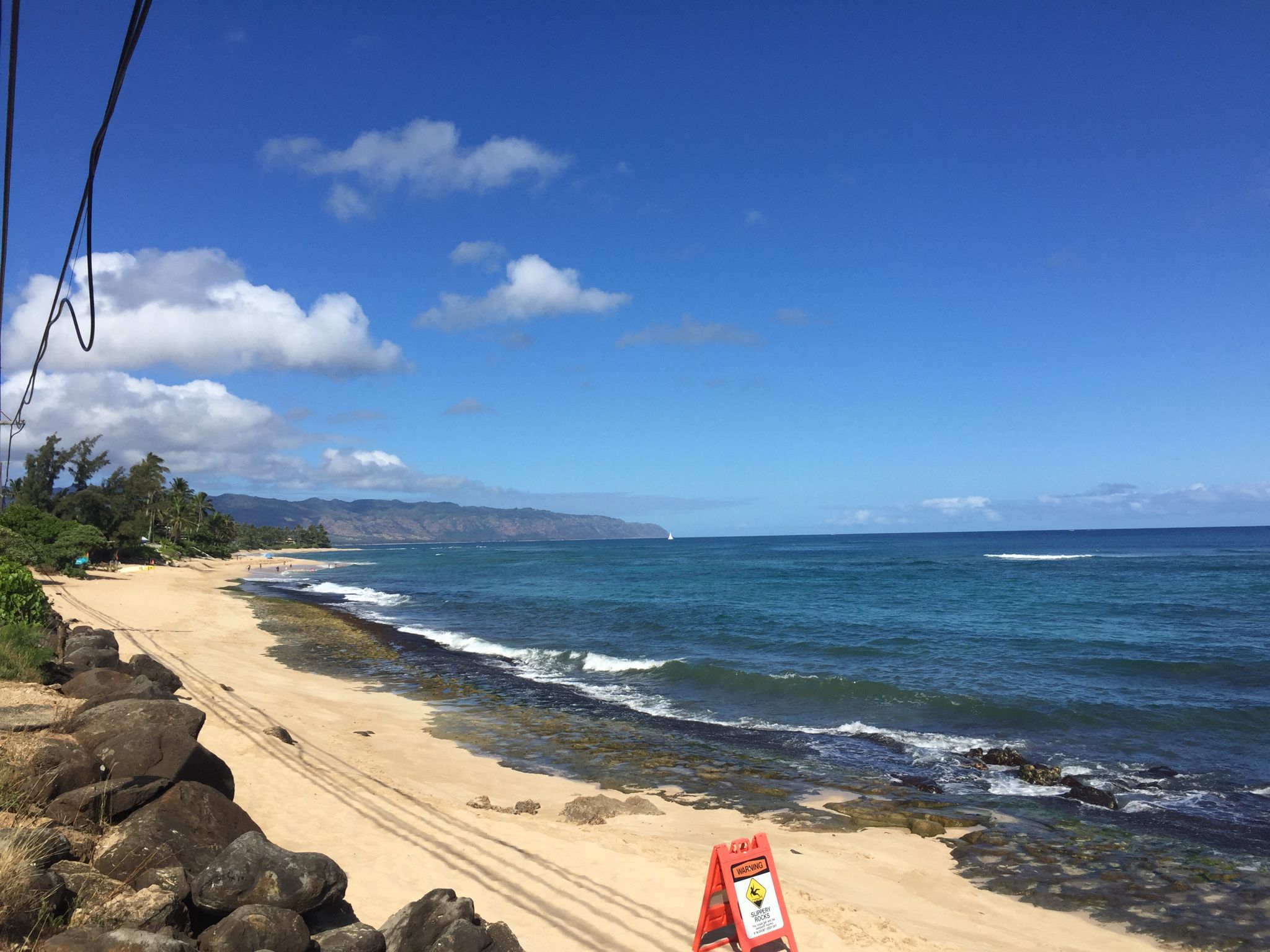 Wide sandy beach with tire tracks, blue ocean, and distant green hills. - Opaeula Road via Paalaa Uka Pupukea Rd loop