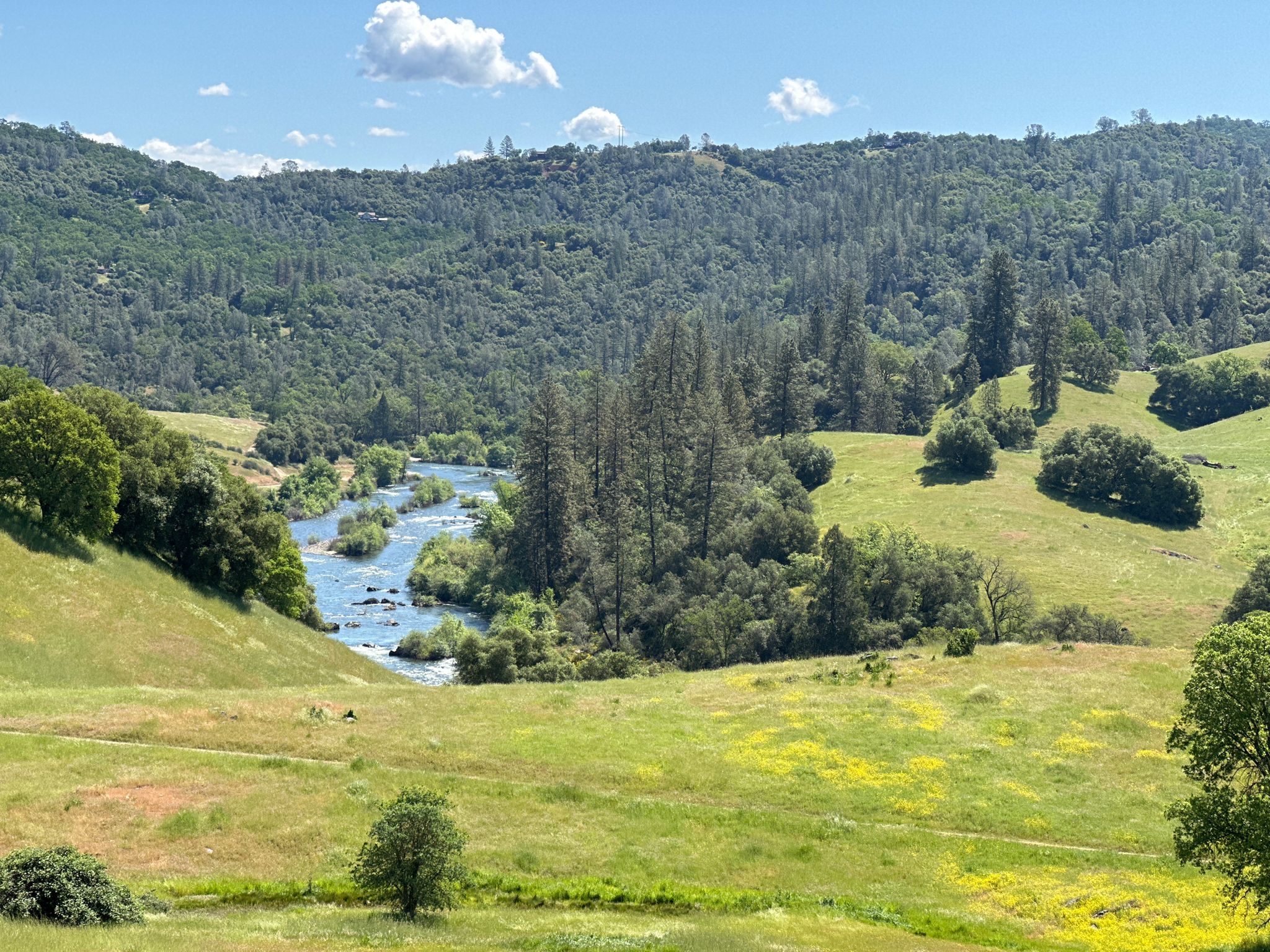 A winding river flows through a lush green valley under a bright sky. - Acorn Creek Trail – Acorn Creek Trail loop from Brush Creek Ranch