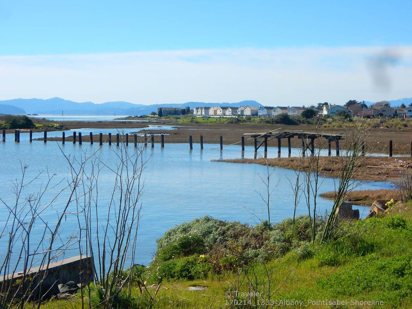 Calm water with old pier pilings, houses, and distant mountains. - Richmond Bay Trail – Shimada Friendship Park loop from Rosie the Riveter/World War II Home Front National Historical Park