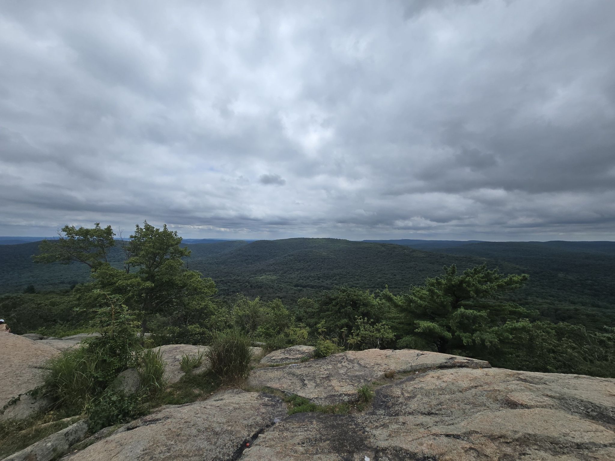 Overcast sky above vast green forested hills from a rocky summit. - Viewpoint – Perkins Memorial Tower loop from Bear Mountain State Park