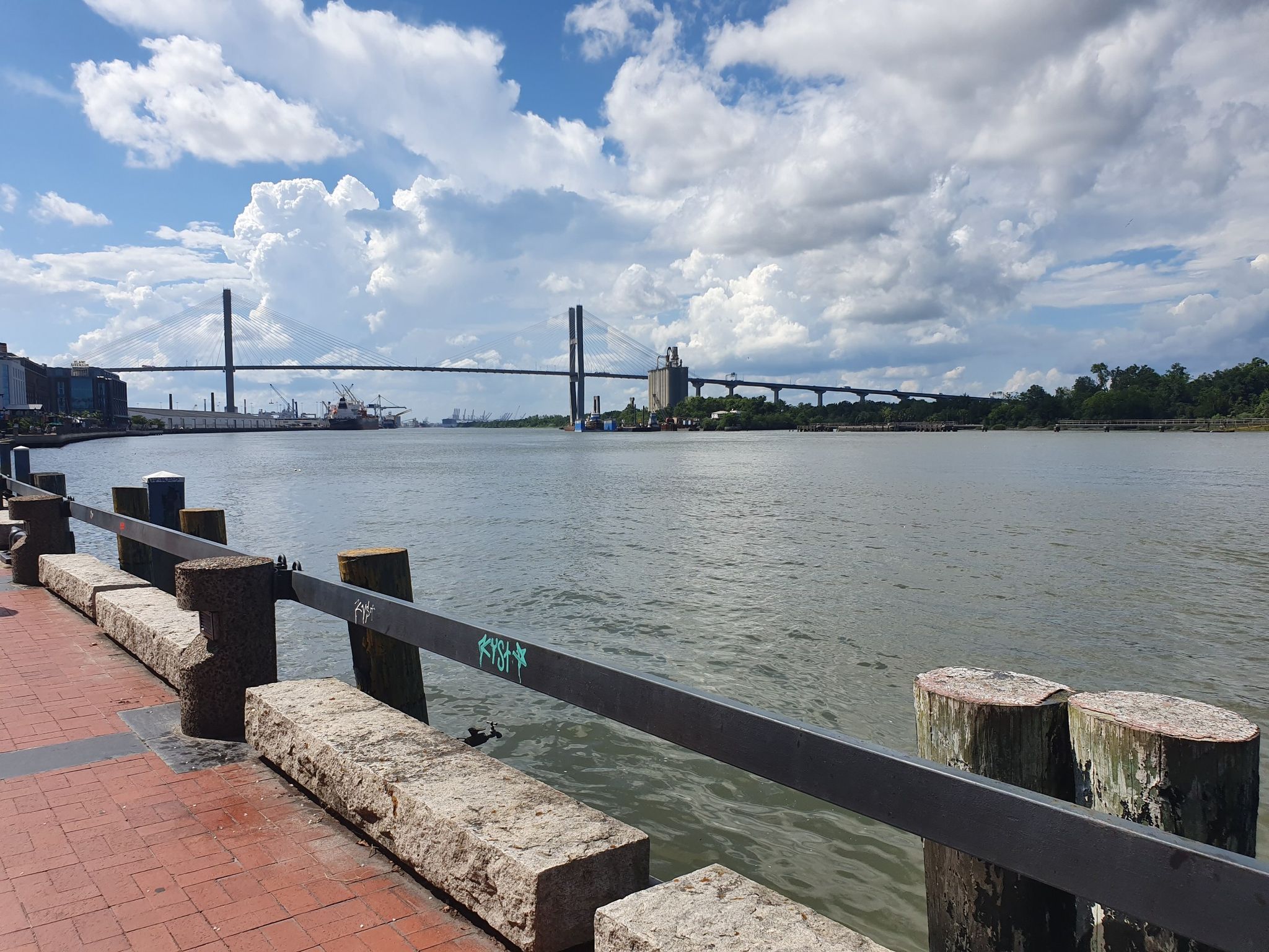 Riverfront with a large cable-stayed bridge under a partly cloudy sky. - Savannah Riverfront