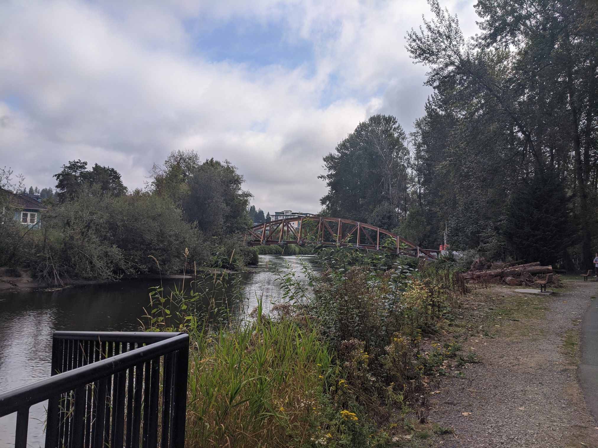 Overcast sky above a river with a wooden truss bridge and lush green banks. - Bothell Landing Trail