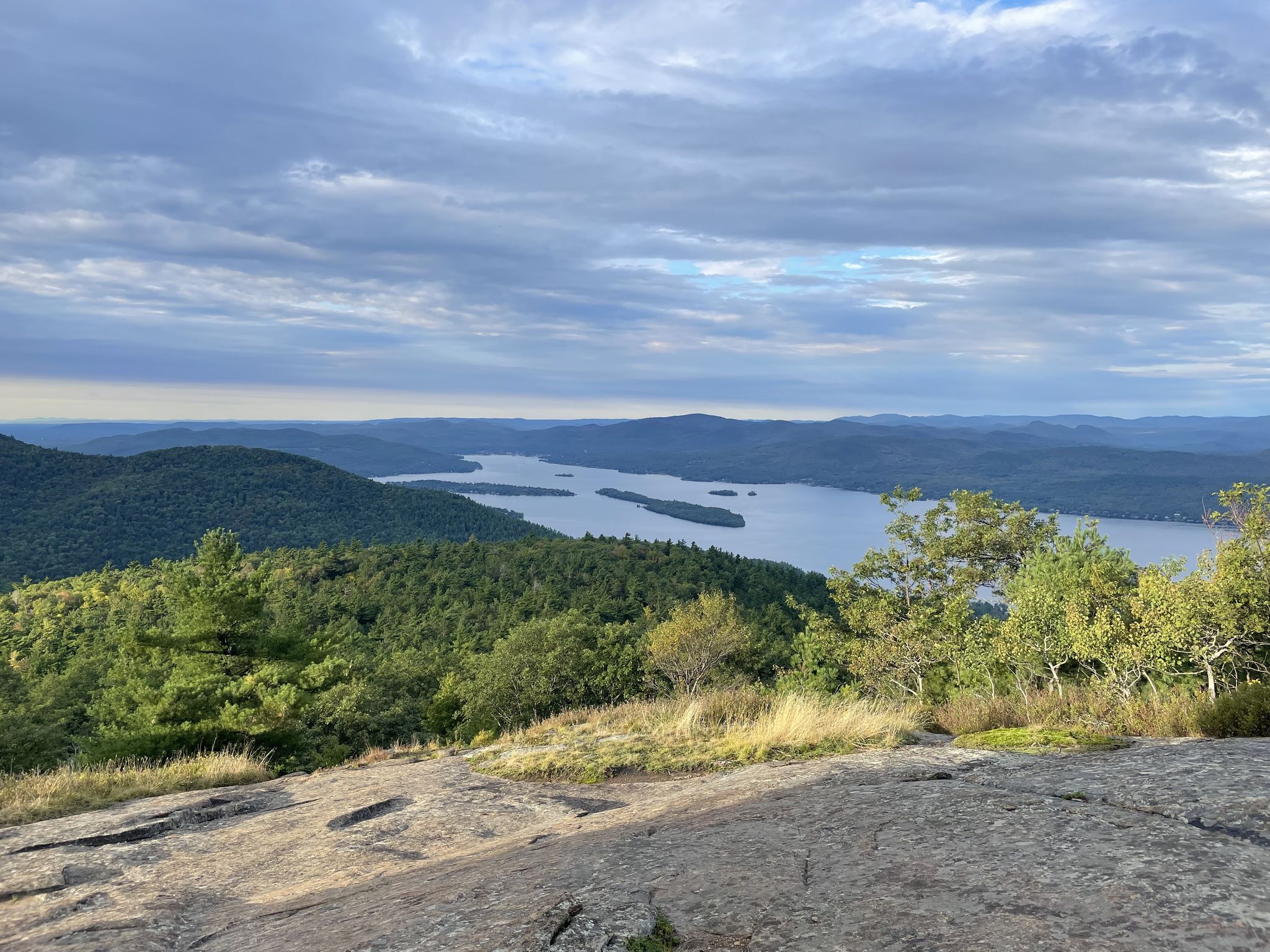 Overcast view of a large lake nestled among green forested mountains. - Buck Mt from Pilot Knob Trail