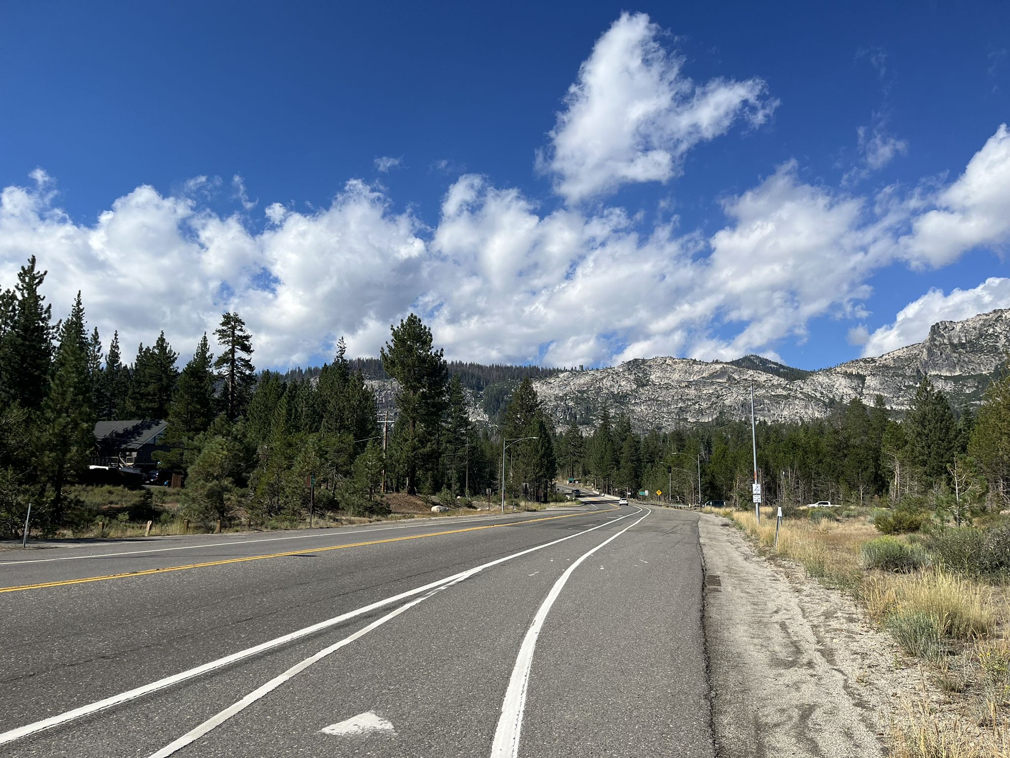 Paved road curves through a forest with rocky mountains under a bright sky. - Hope Valley Wildlife Area – Luther Pass loop from High Meadows Trailhead parking lot