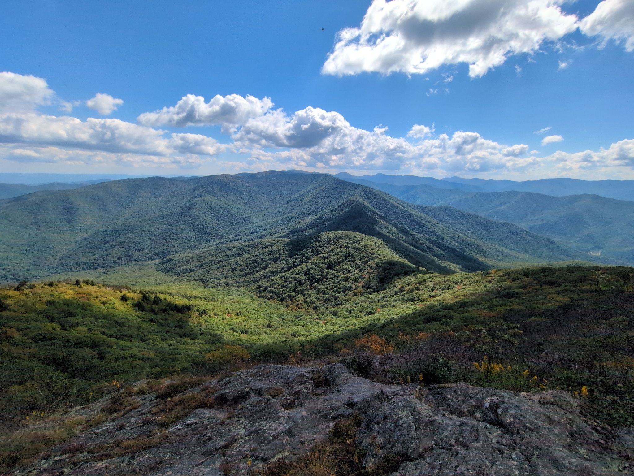 Expansive view of green mountains from a rocky foreground under blue sky. - Cold Mountain via Art Loeb Trail