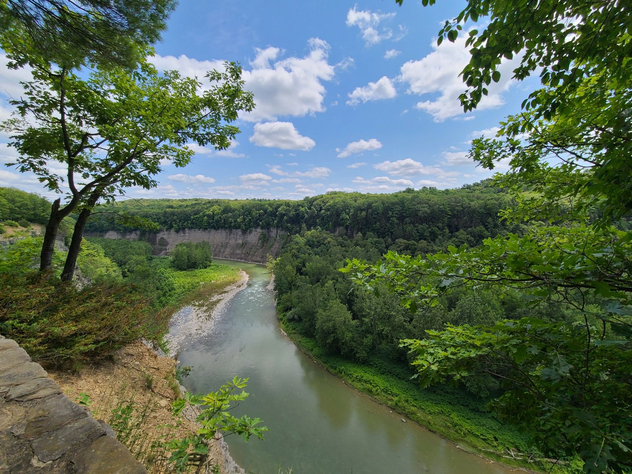 River winding through a lush green gorge under a bright blue sky. - Great Bend Overlook – Archery Field Overlook loop from Letchworth State Park