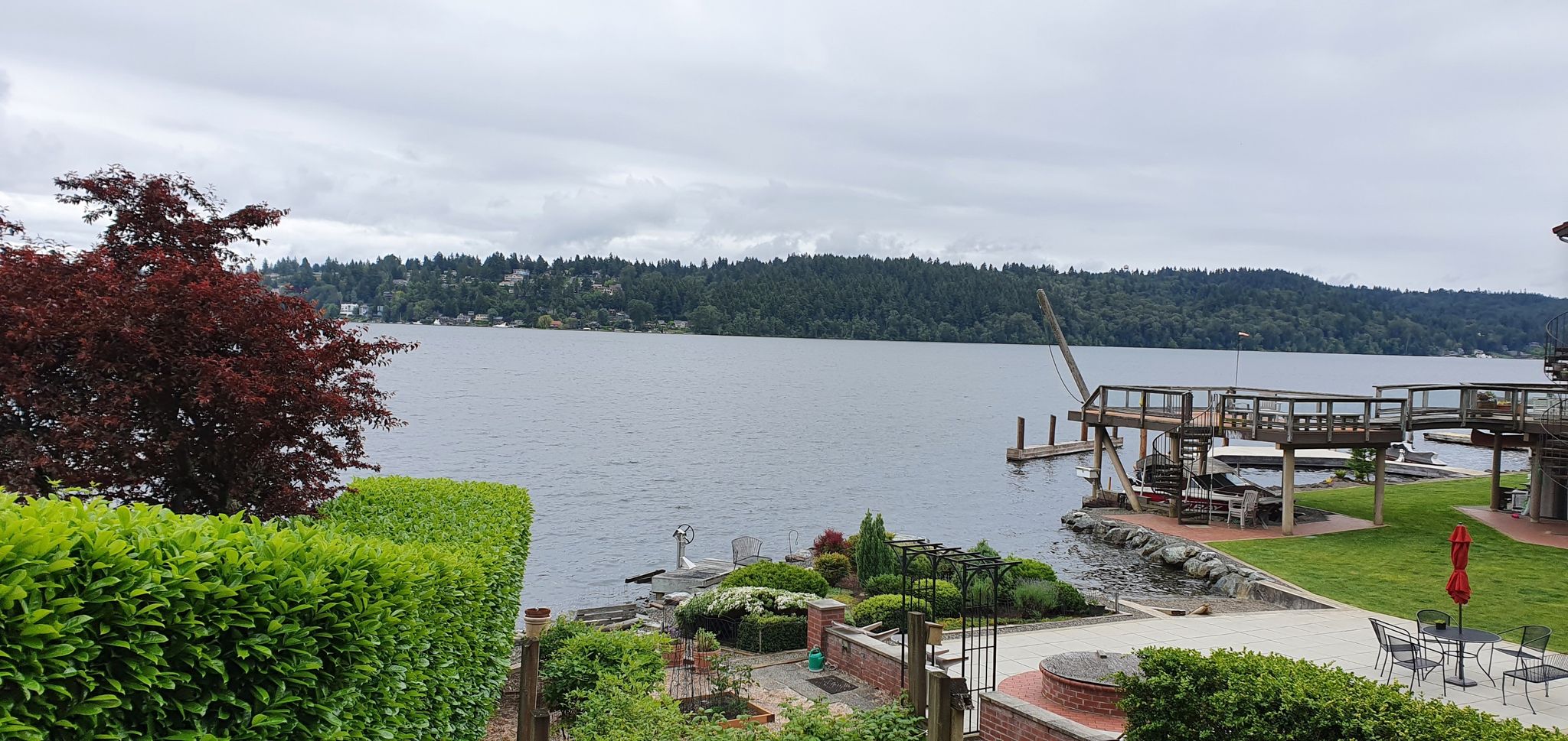 Lake view from a garden patio with distant forested shores under cloudy sky. - 192 Brewing Company – Floodwater reservoir loop from Bothell