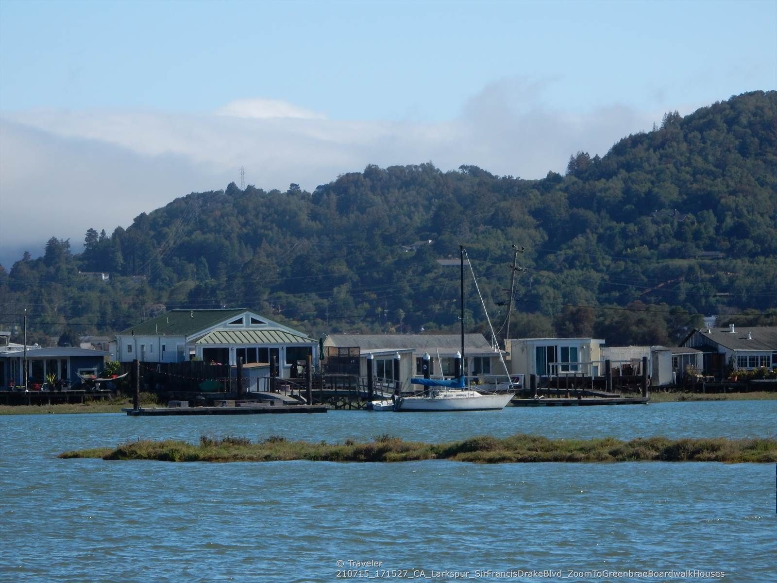 Houseboats and a sailboat on calm water with forested hills under a cloudy sky. - San Francisco Bay Trail