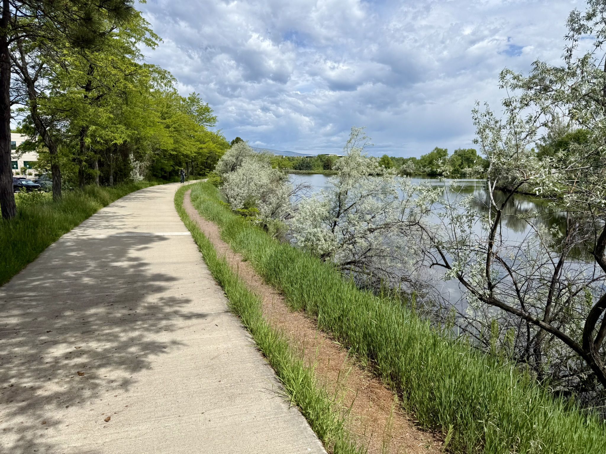 A paved path curves alongside a tranquil lake under a cloudy sky. - South Boulder Creek Trail – Centennial Trail loop from Eldorado Springs