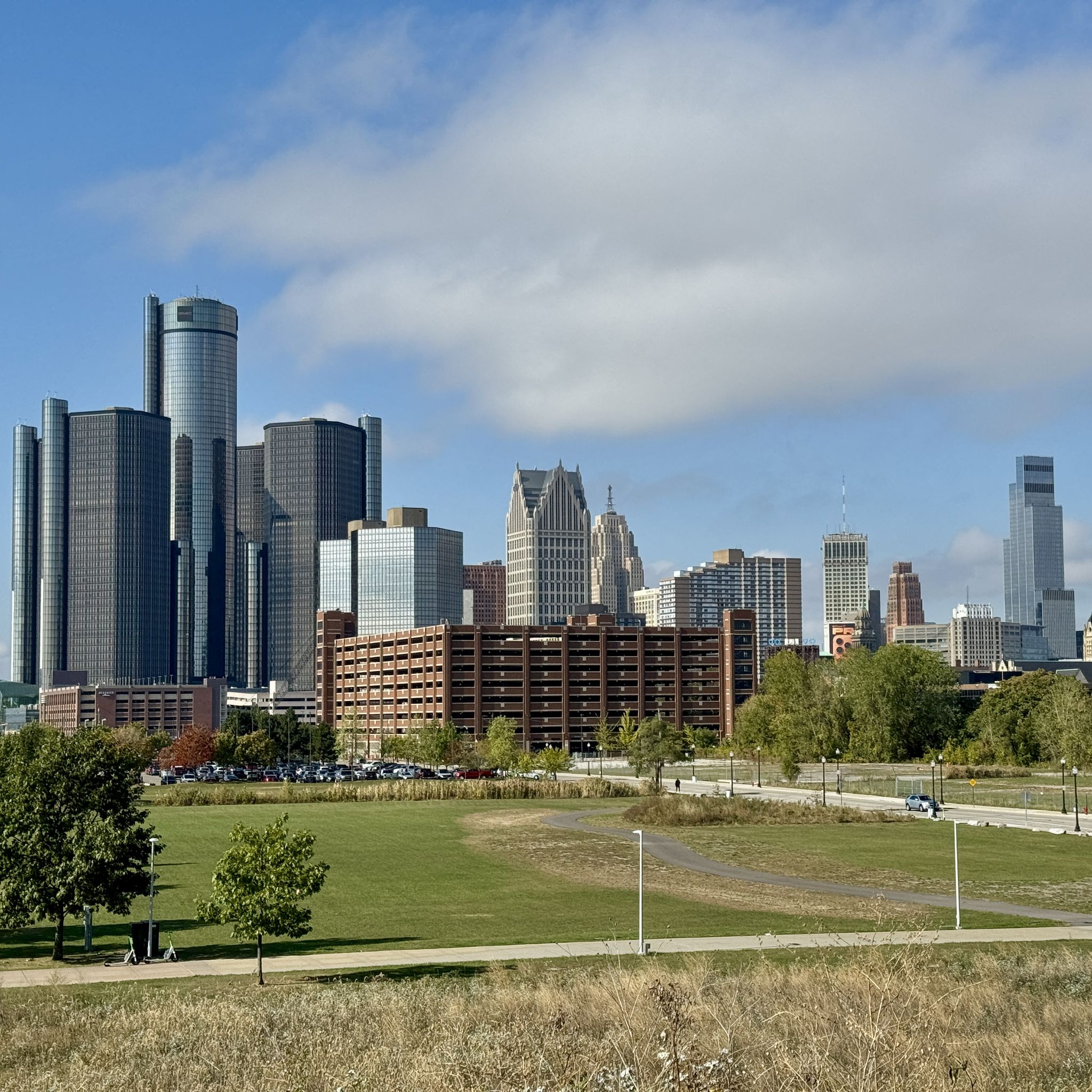 Modern city skyline rises behind a large, vibrant green park. - Detroit Riverwalk and Dequindre Cut Loop