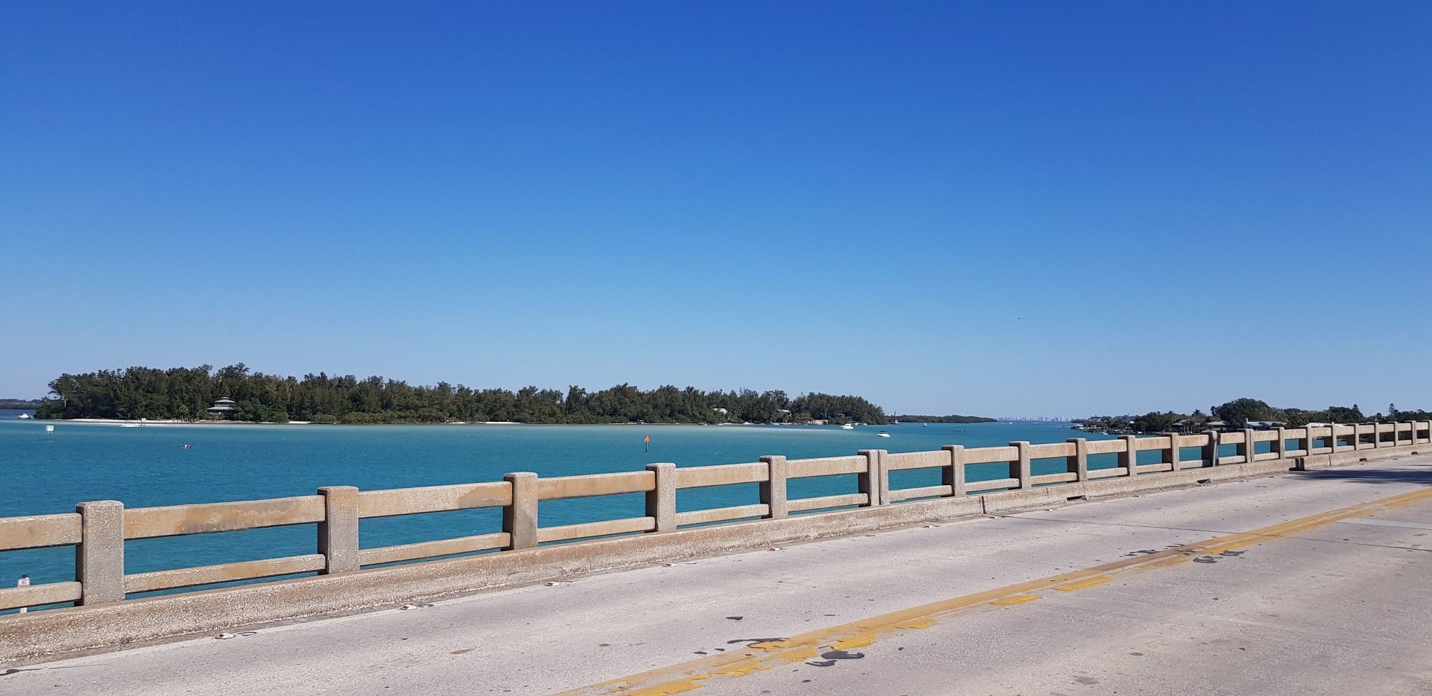 Concrete bridge railing overlooks calm turquoise water and a distant green island. - Bayfront Park Sarasota – John Ringling Bridge loop from IMG Academy