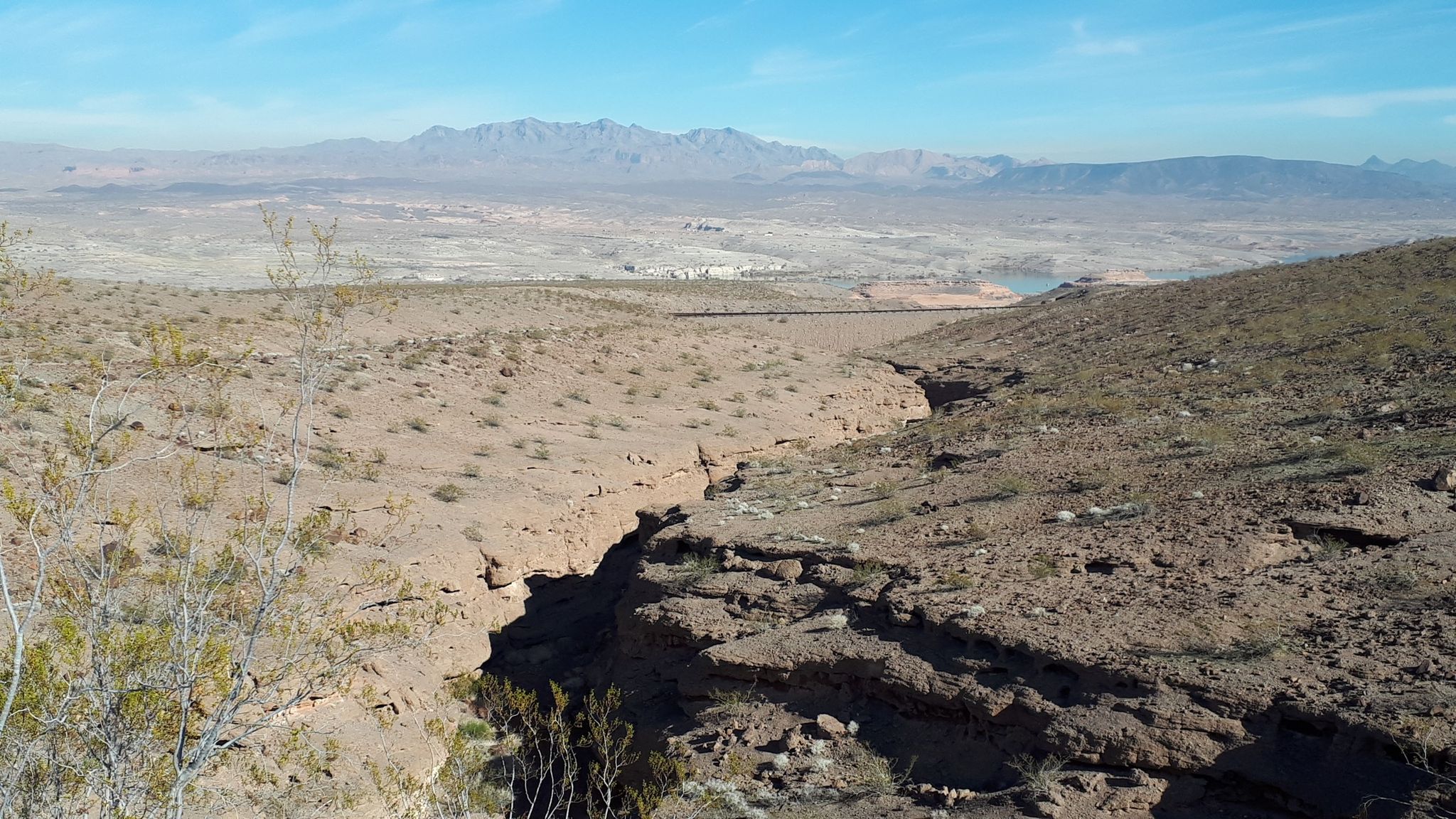 Deep dry wash in a vast desert landscape with distant mountains under clear sky. - White Owl Canyon Trail