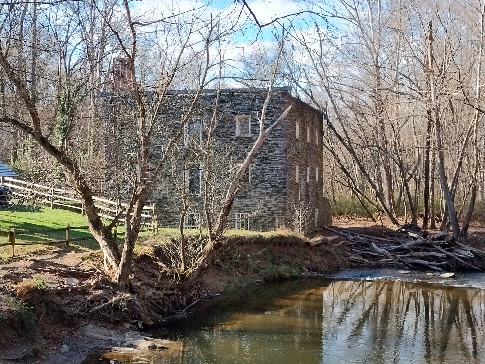 Sunlit stone building next to a river with bare trees and a wooden fence. - Seneca Ridge and Seneca Greenway Trail Loop