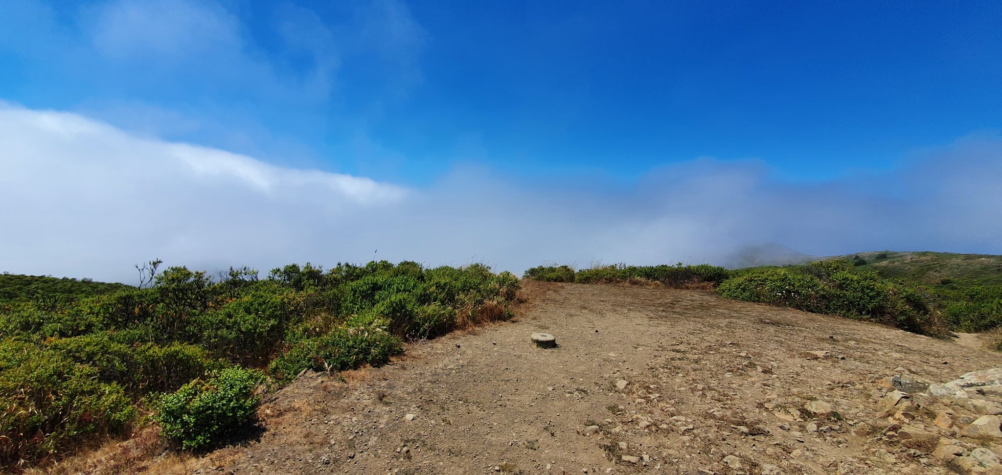 Open dirt clearing on a hilltop with fog rolling in. - Coyote Ridge Trail to Muir Beach