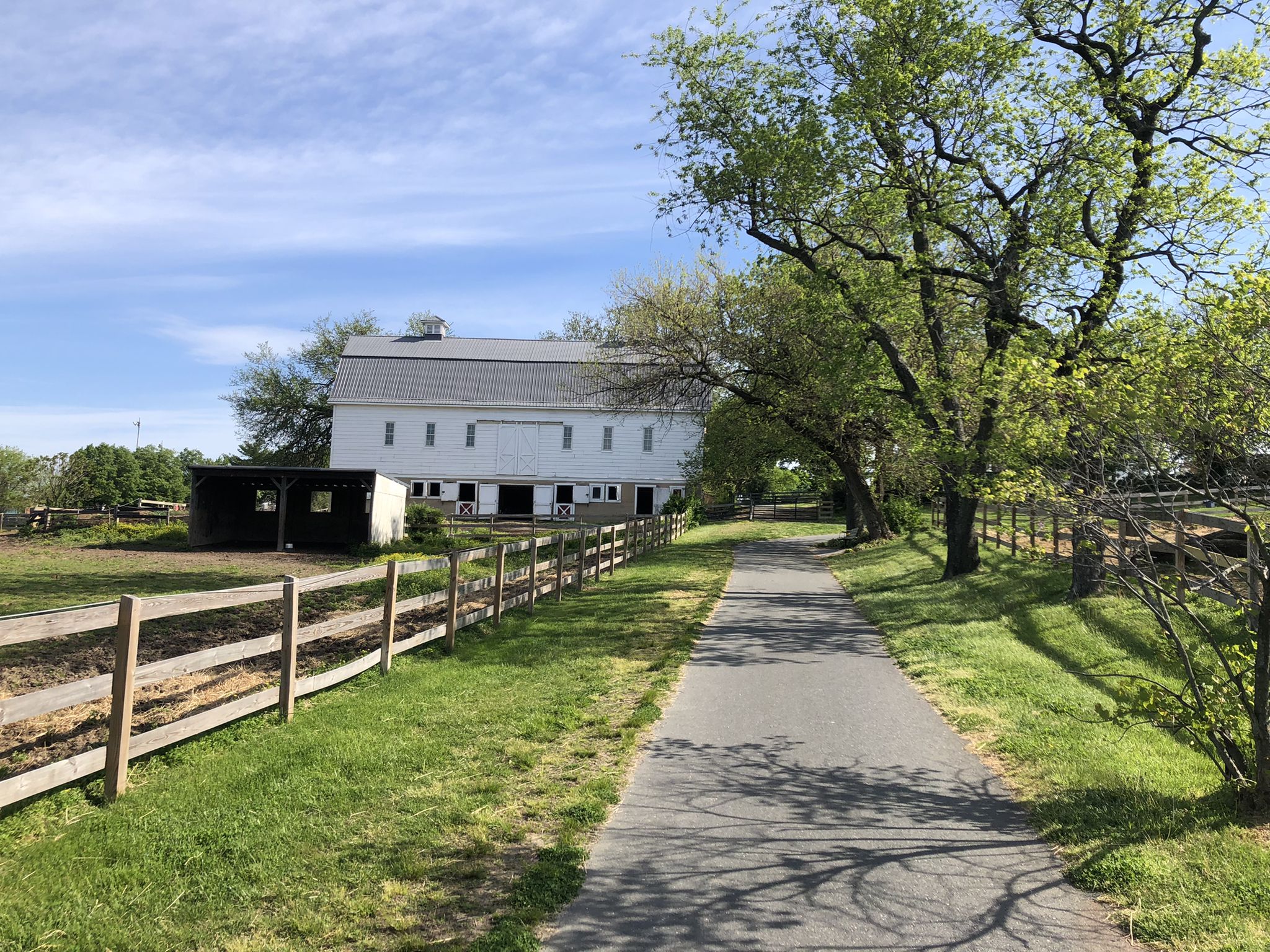Paved path next to a white barn and wooden fence on a sunny day. - Roadbike loop from Saint Denis