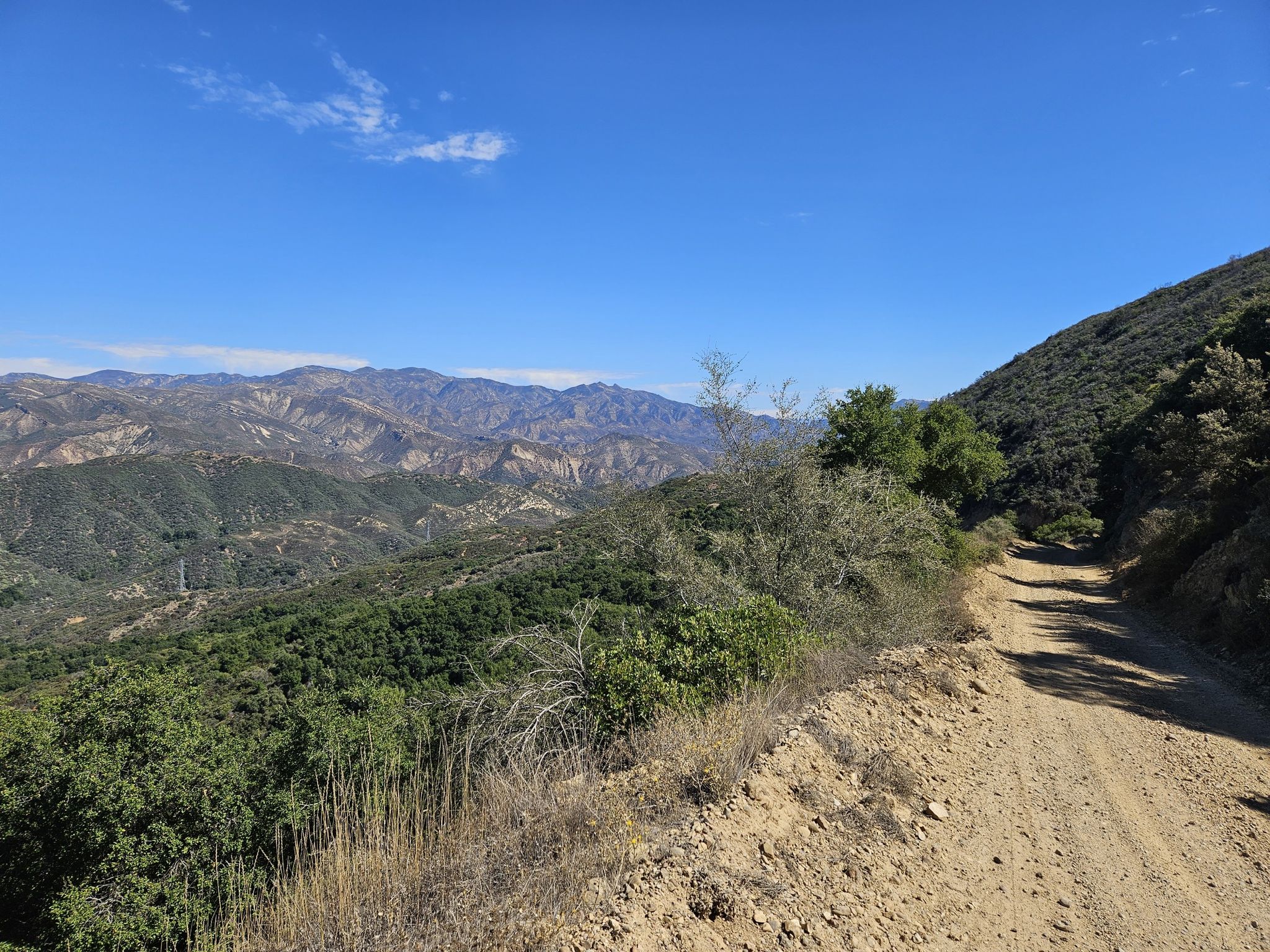 A sunny dirt road winds along a mountain ridge with distant peaks. - Blue Canyon and Romero Trail Loop