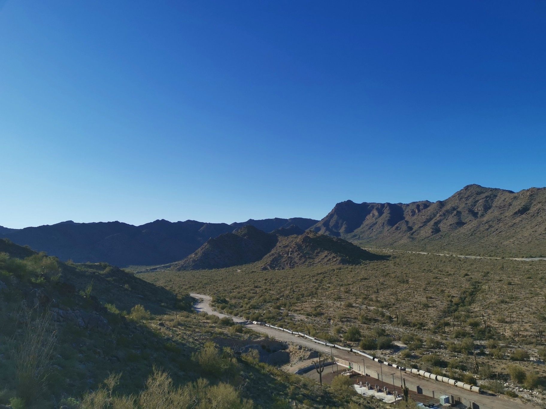 Desert valley with a winding road and rugged mountains under a clear sky. - Verrado Mountain Loop