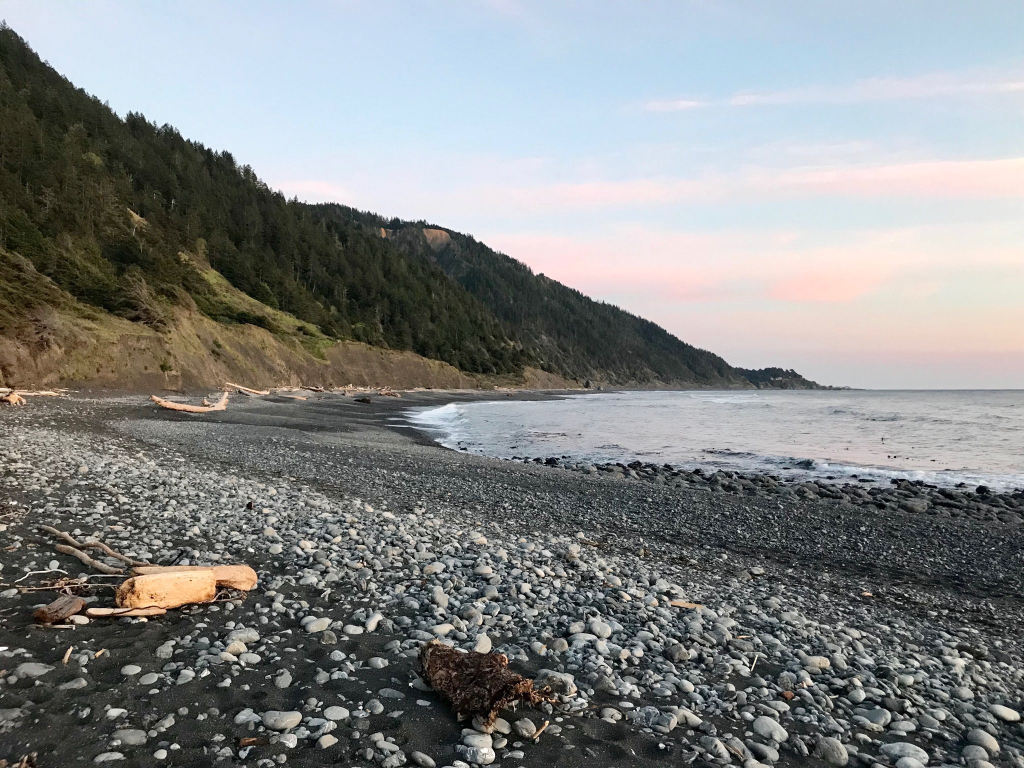 Rocky beach with driftwood and forested hills at a soft sunset. - Black Sands Beach loop from Gitchell Creek