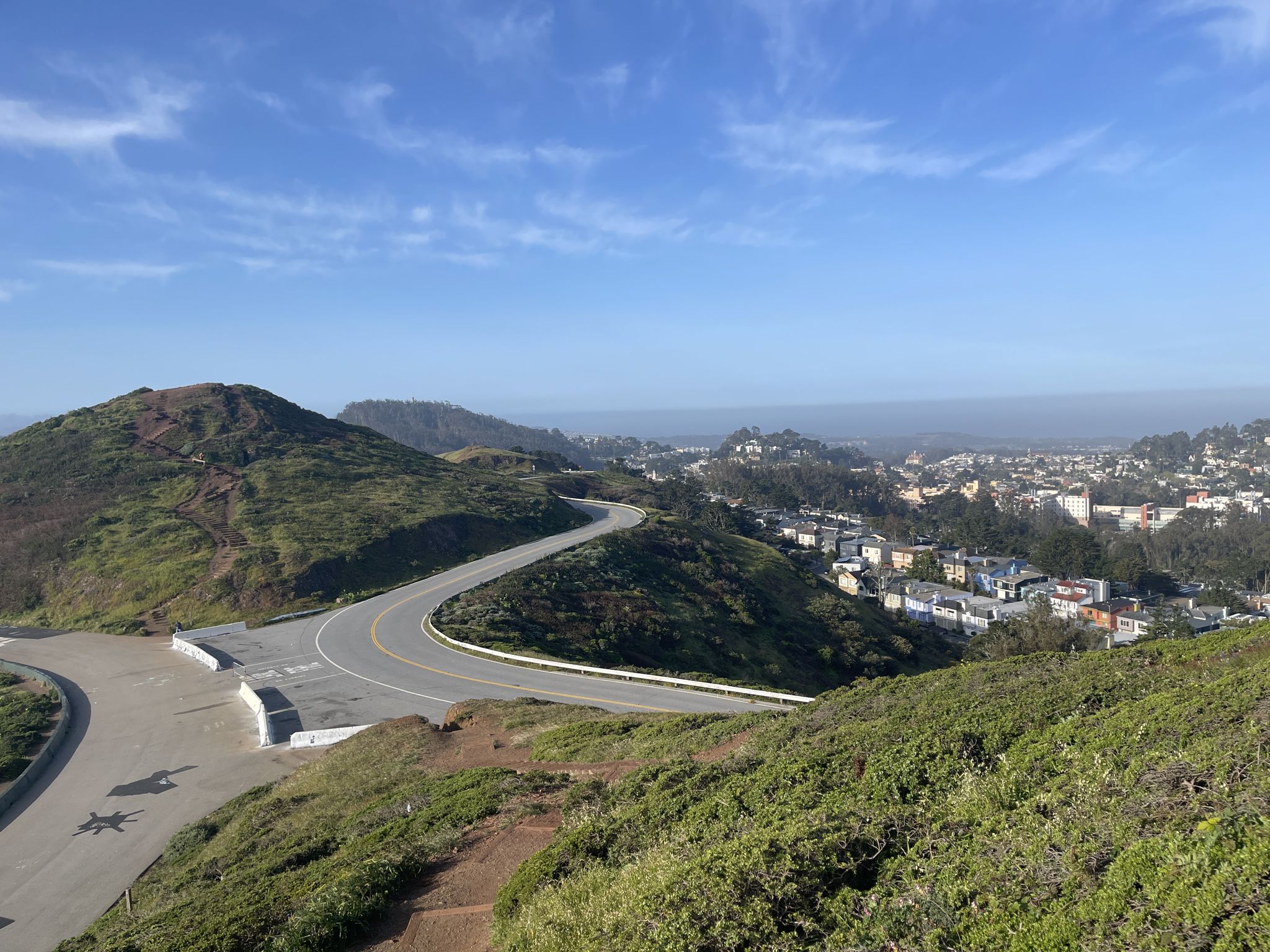 Winding road through green hills, with a distant city under blue sky. - Laguna Honda Lake – Christmas Tree Viewpoint loop from Judah Street & 28th Avenue