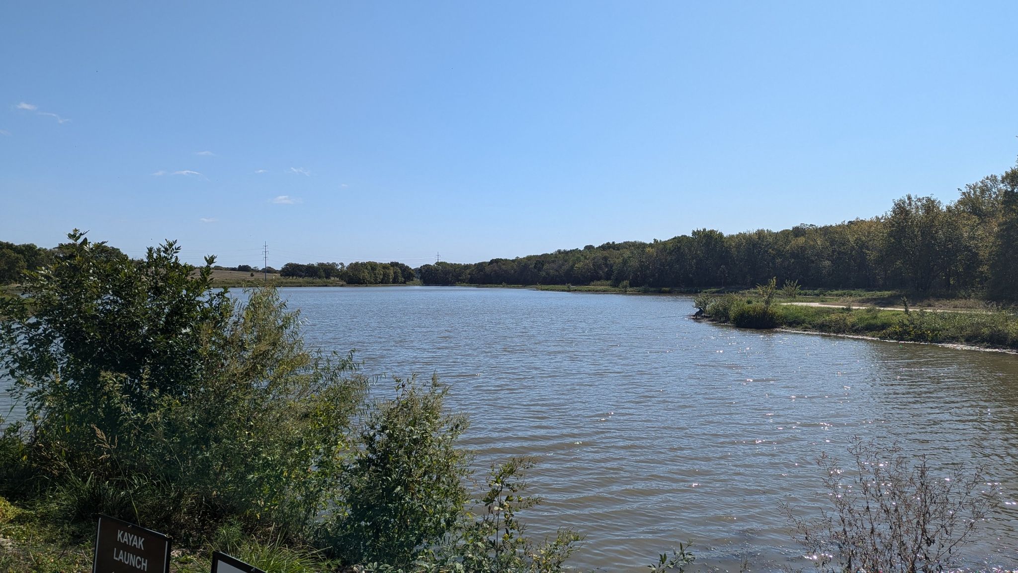 A wide lake surrounded by green trees under a clear blue sky. - Oak Point and Bob Woodruff Parks Loop
