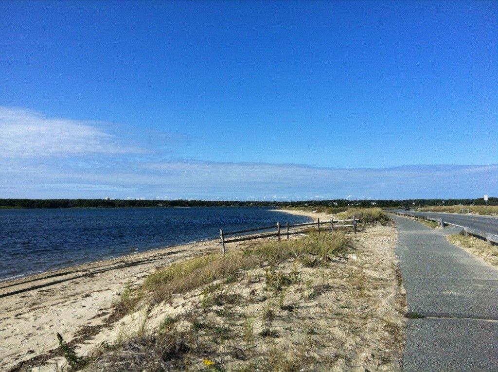 Calm bay beside a sandy beach, grassy dunes, and a paved road. - Joseph Sylvia State Beach – Historic Edgartown loop from Edgartown