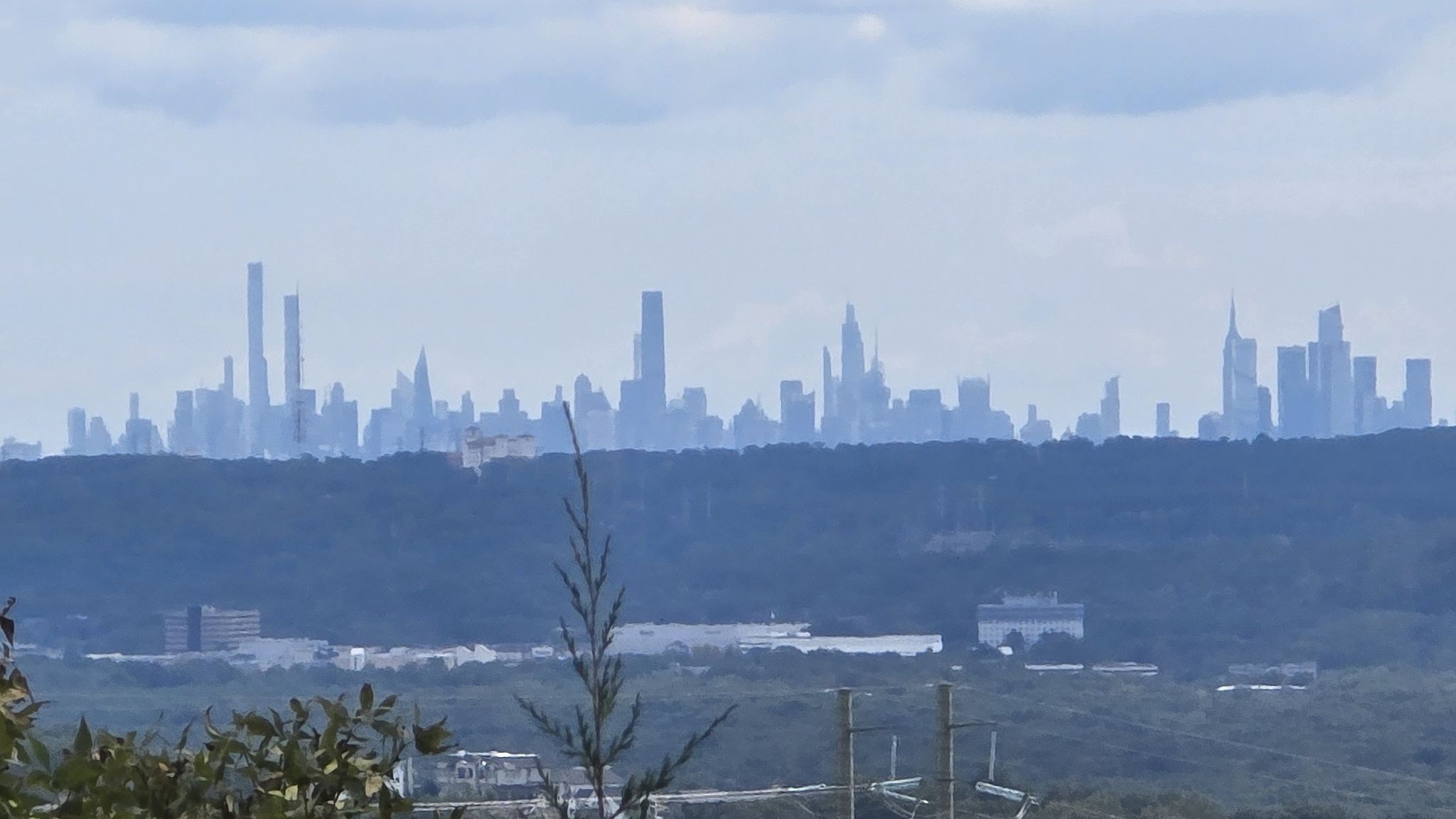 Distant city skyline visible above a forested landscape on a cloudy day. - Lake Valhalla Overlook via Yellow, Orange, and Green Dot Trails
