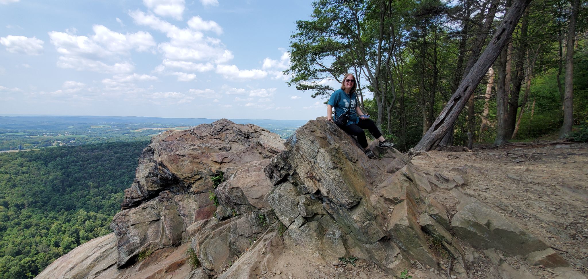 Person sits on rocky outcrop overlooking a vast green valley on a sunny day. - Hawk Rock via Appalachian Trail