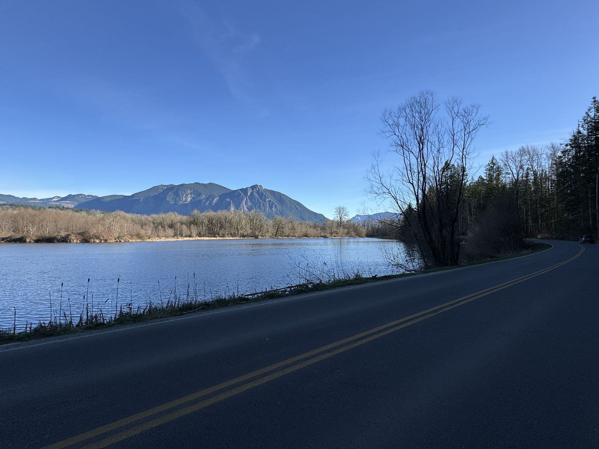 Paved road alongside a calm lake with mountains under a clear blue sky. - Snoqualmie Valley Trail Loop