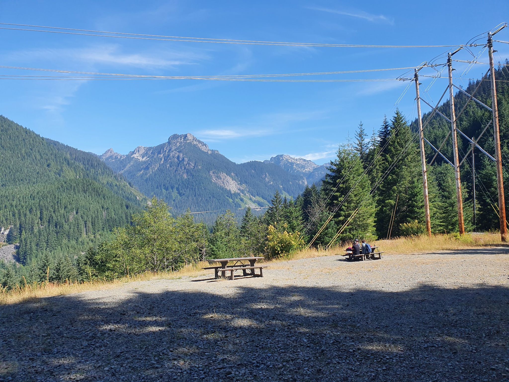 People at picnic tables in a sunny clearing overlooking a forested mountain valley. - Snoqualmie Tunnel – Snoqualmie Pass loop from Change Peak
