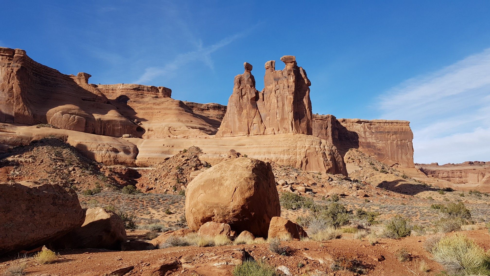 Towering red rock spires dominate a sunny desert landscape with large boulders. - La Sal Mountains Viewpoint – Courthouse Towers Viewpoint loop from La Sal Mountains Viewpoint