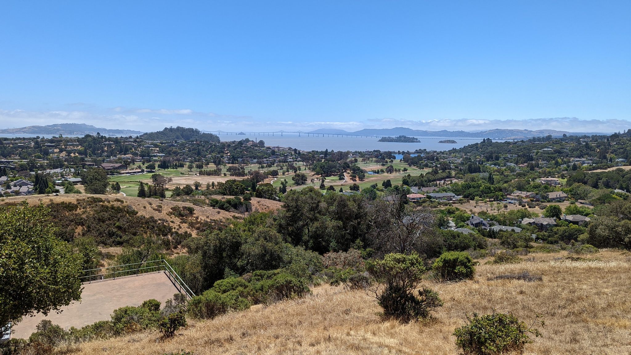 Overlook of a town, golf course, and distant water under a clear sky. - China Camp State Park Village – Bay View Trail loop from McNears Beach