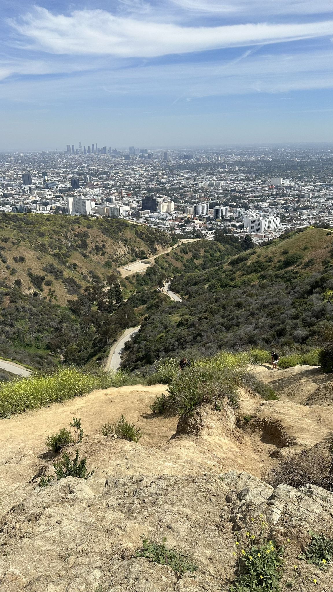 Steep dirt path descends into a valley with a city skyline in the distance. - Runyon Canyon Park loop from Hollywood Curson