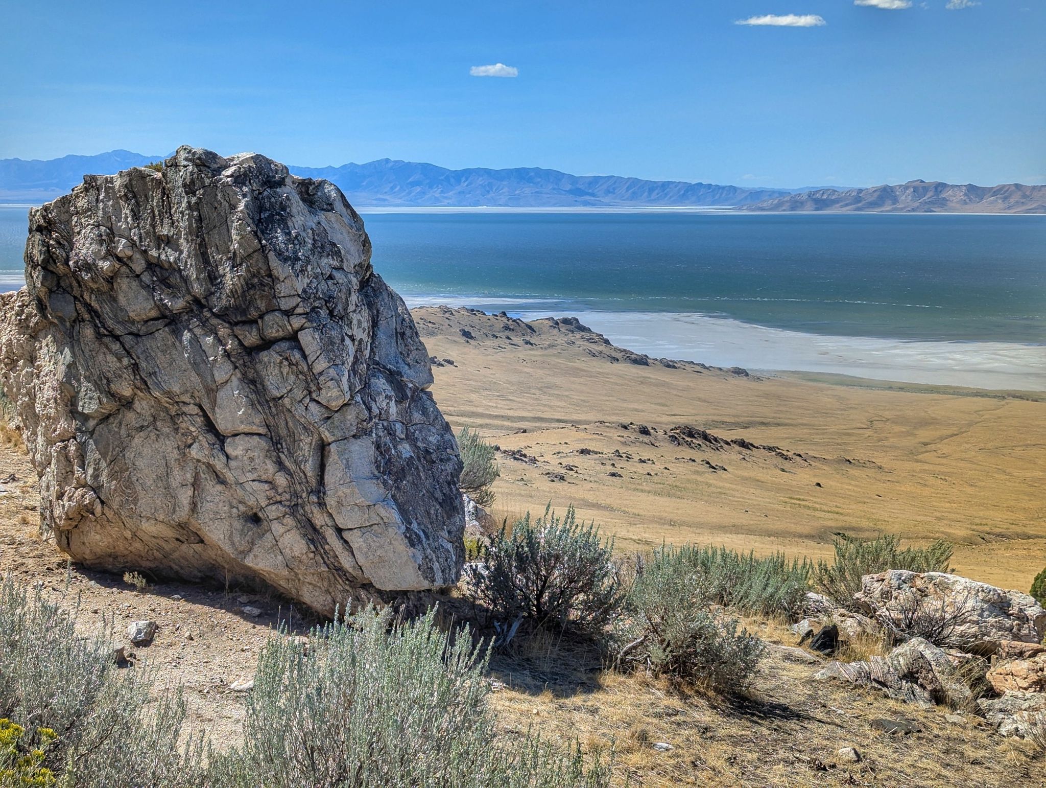 A large rock sits on a dry hill overlooking a wide blue lake. - Sentry Loop Trail