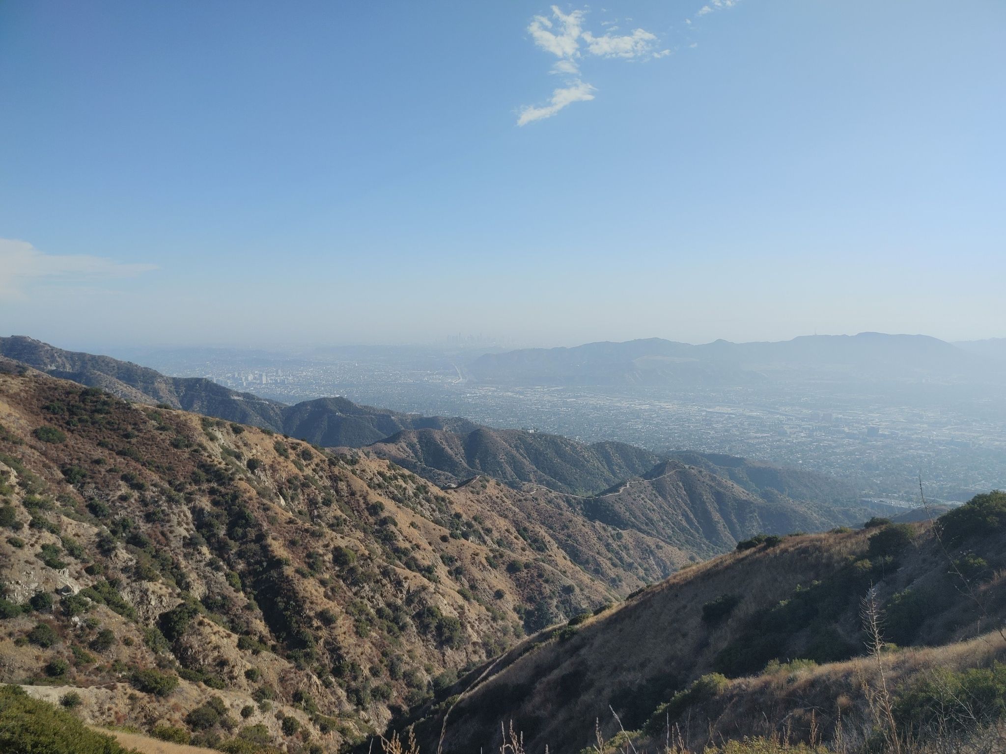 Expansive view of dry, rugged mountains overlooking a hazy distant city under blue sky. - Verdugo Peak loop from Downtown Burbank