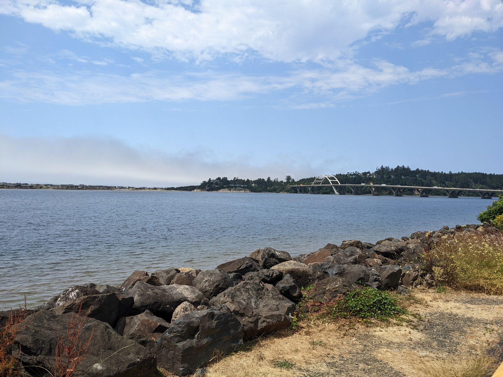Wide shot of a calm bay with a distant bridge under a bright sky. - Oregon Coast Scenic Bikeway