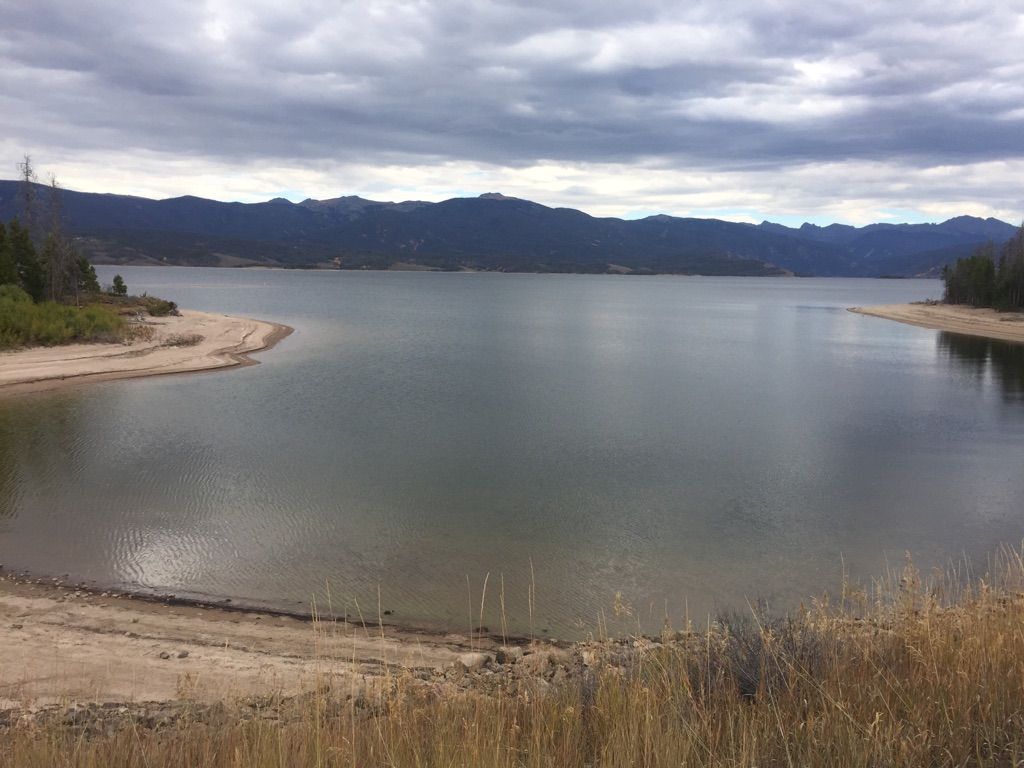 Large lake with sandy shores and distant mountains under an overcast sky. - RMNP/Alpine Visitor Center