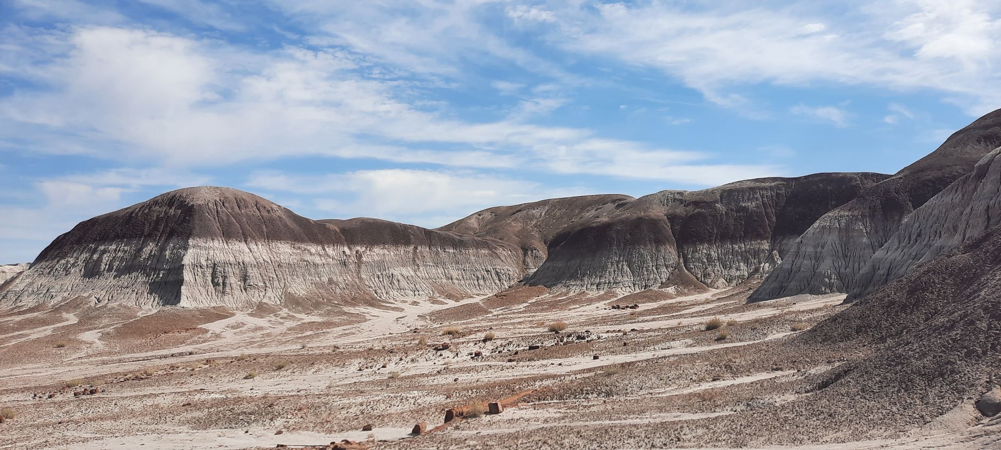 Arid landscape with layered, multi-colored hills under a bright, cloudy sky. - Long Logs and Agate House Trail