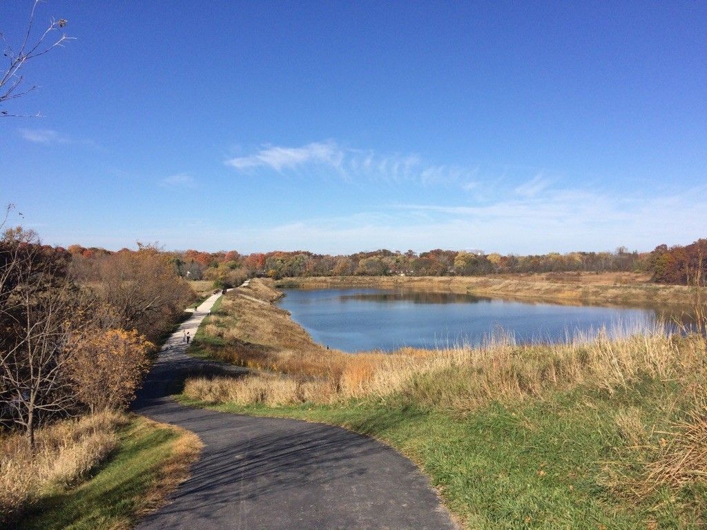 Paved path alongside a lake with autumn trees under a clear sky. - Maple Lake and North Central DuPage Regional Trail Loop