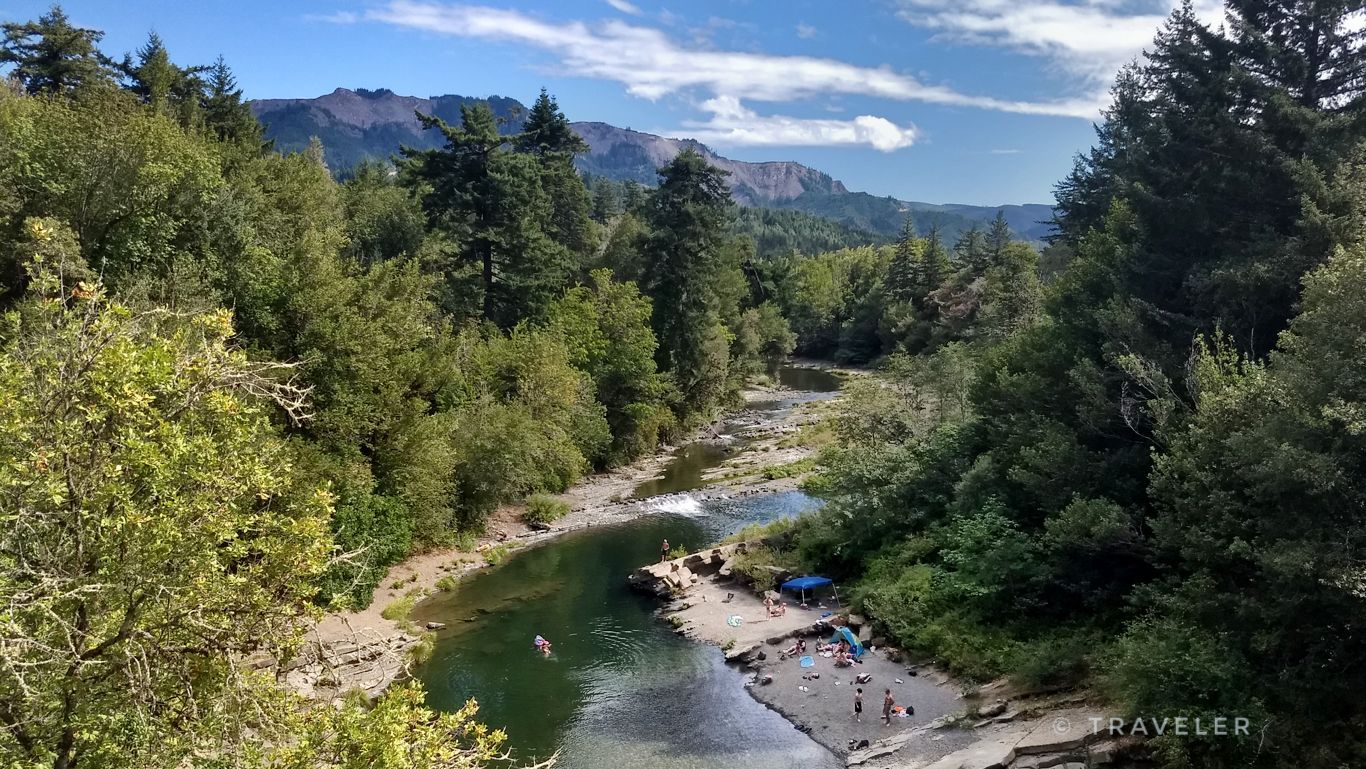 Sunny river winding through a lush forest with people swimming and relaxing. - Johnson Mountain gravel loop