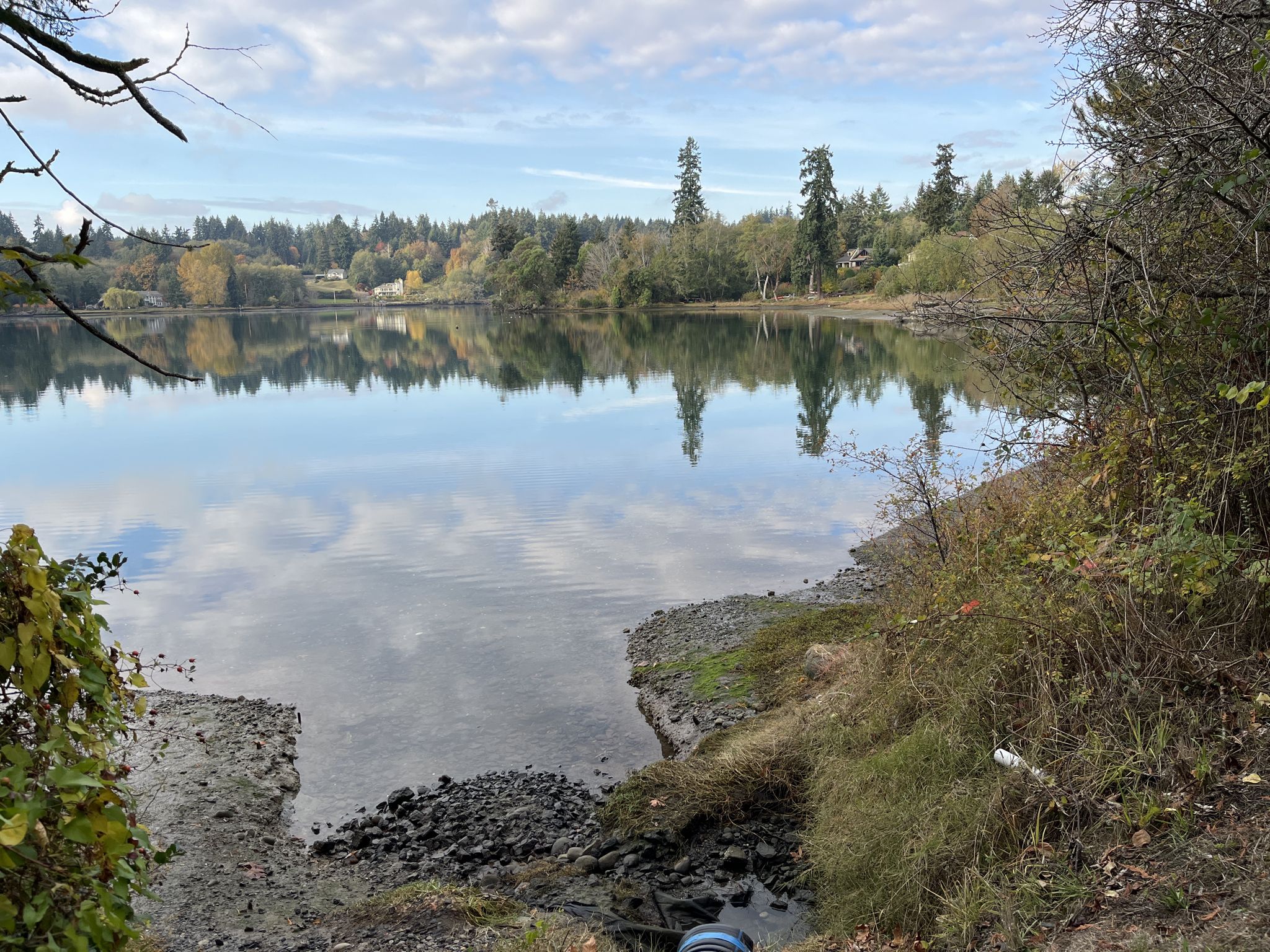 Calm lake reflecting trees and cloudy sky, with a rocky shore. - Waterfront park loop from east ferry terminal