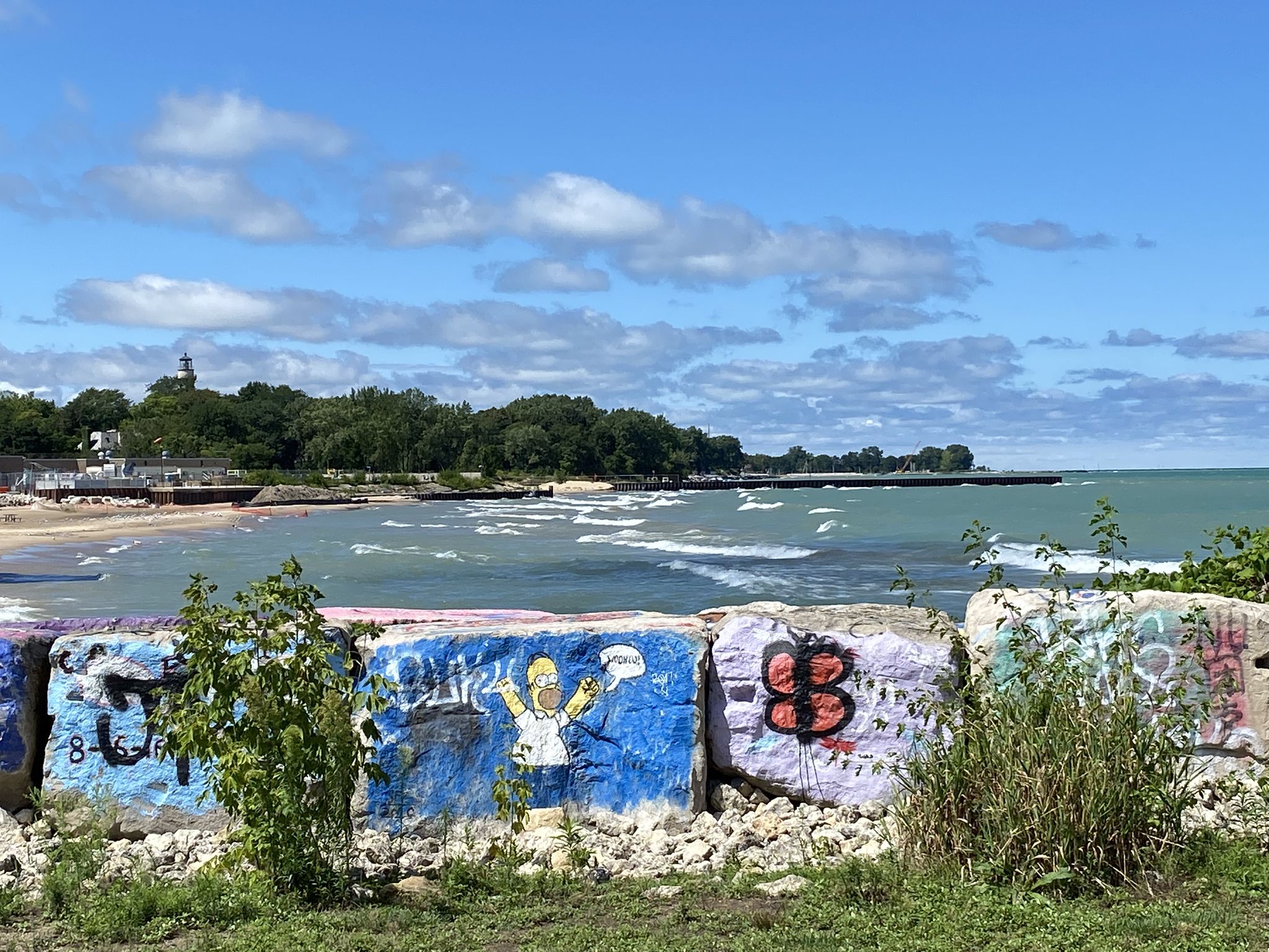 Graffiti-covered blocks in foreground, with a beach and wavy water in the background. - Grosse Point Lighthouse – Green Bay Trail loop from Fort Sheridan